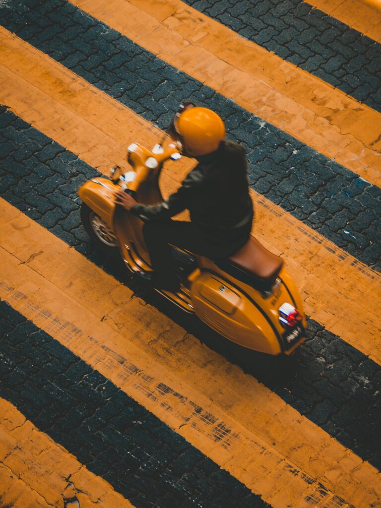 A person rides a yellow scooter across a zebra crossing in an urban setting.